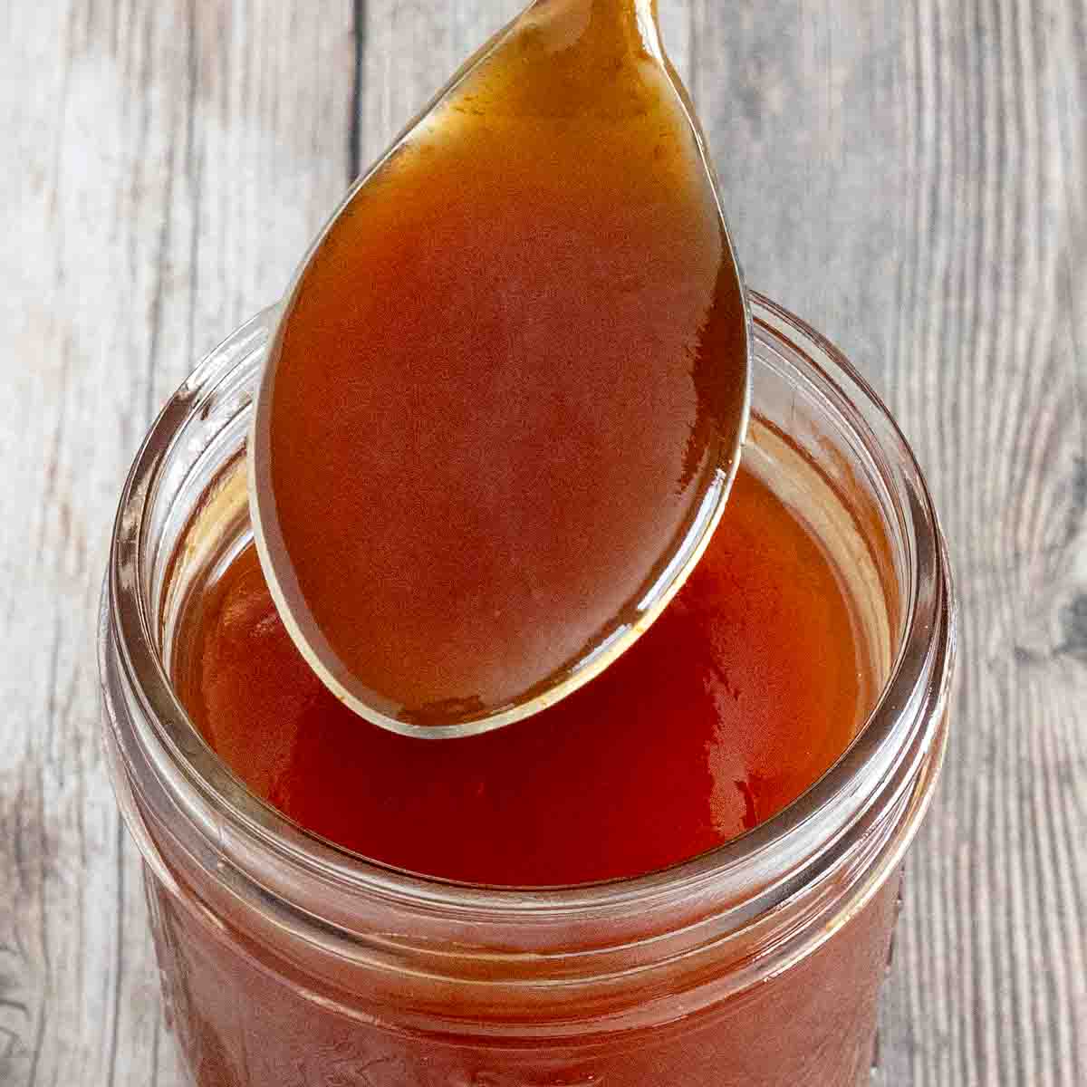 Sweet and sour sauce in a glass jar with a spoon coming out.