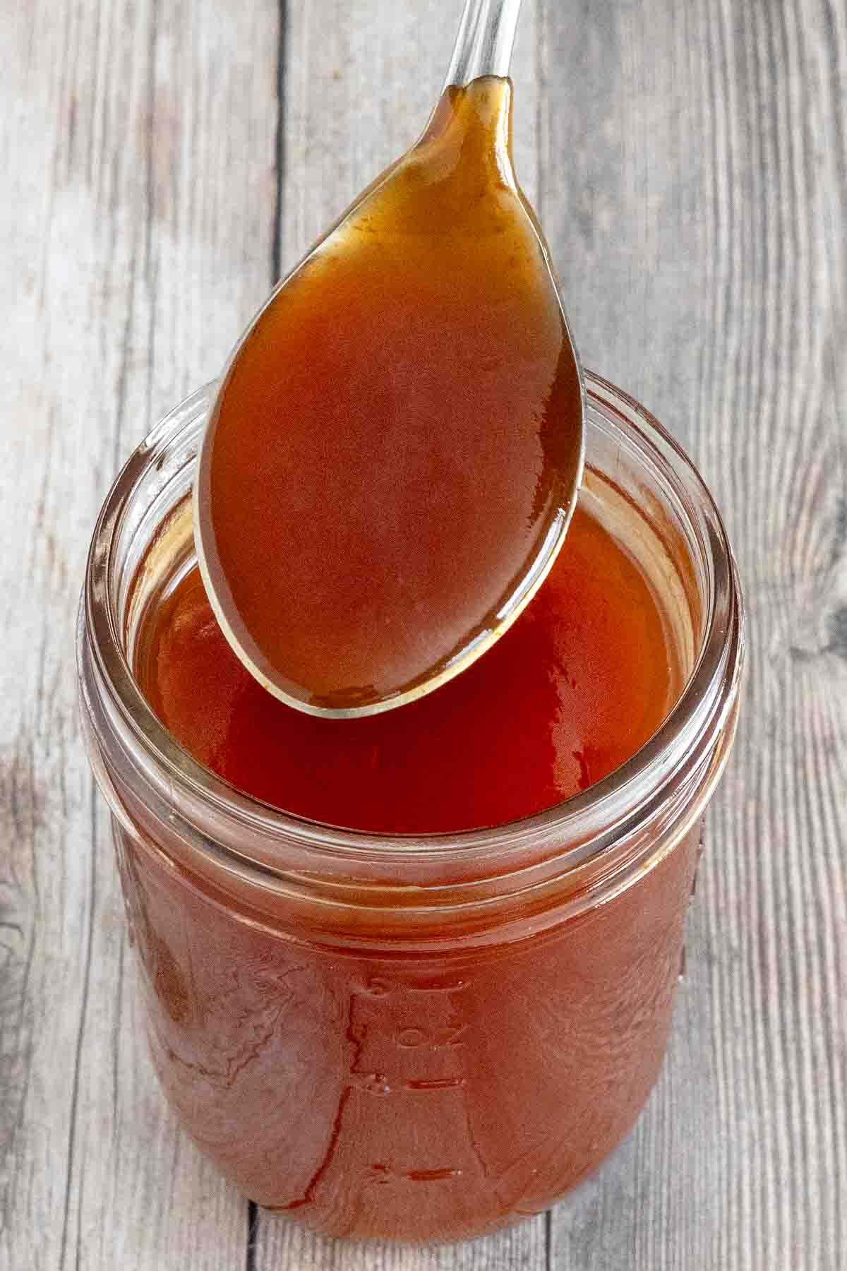 Sweet and sour sauce in a glass jar with a spoon coming out.