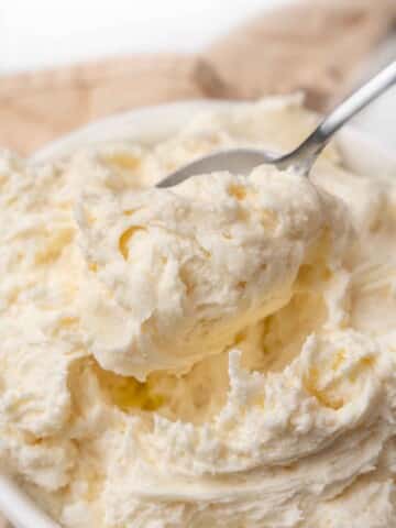 Vanilla buttercream in a white bowl with a spoon coming out.