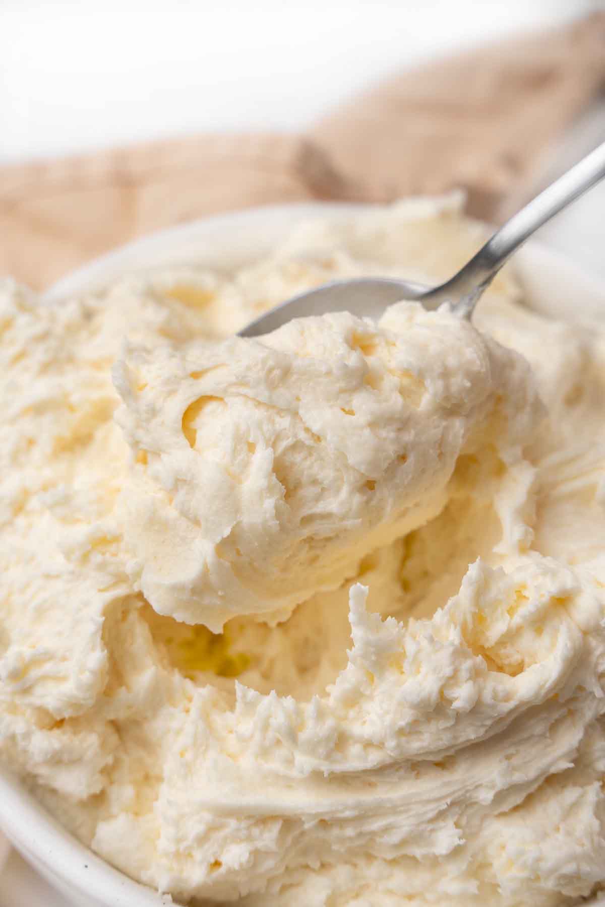 Vanilla buttercream in a white bowl with a spoon coming out.