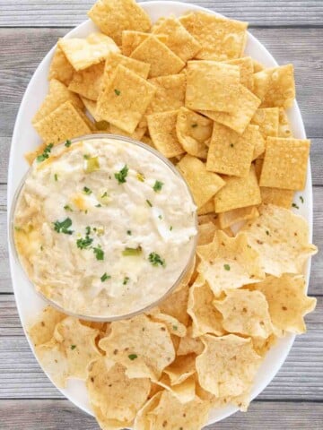 crab rangoon dip in bowl on a white platter with crackers and tortilla dippers.