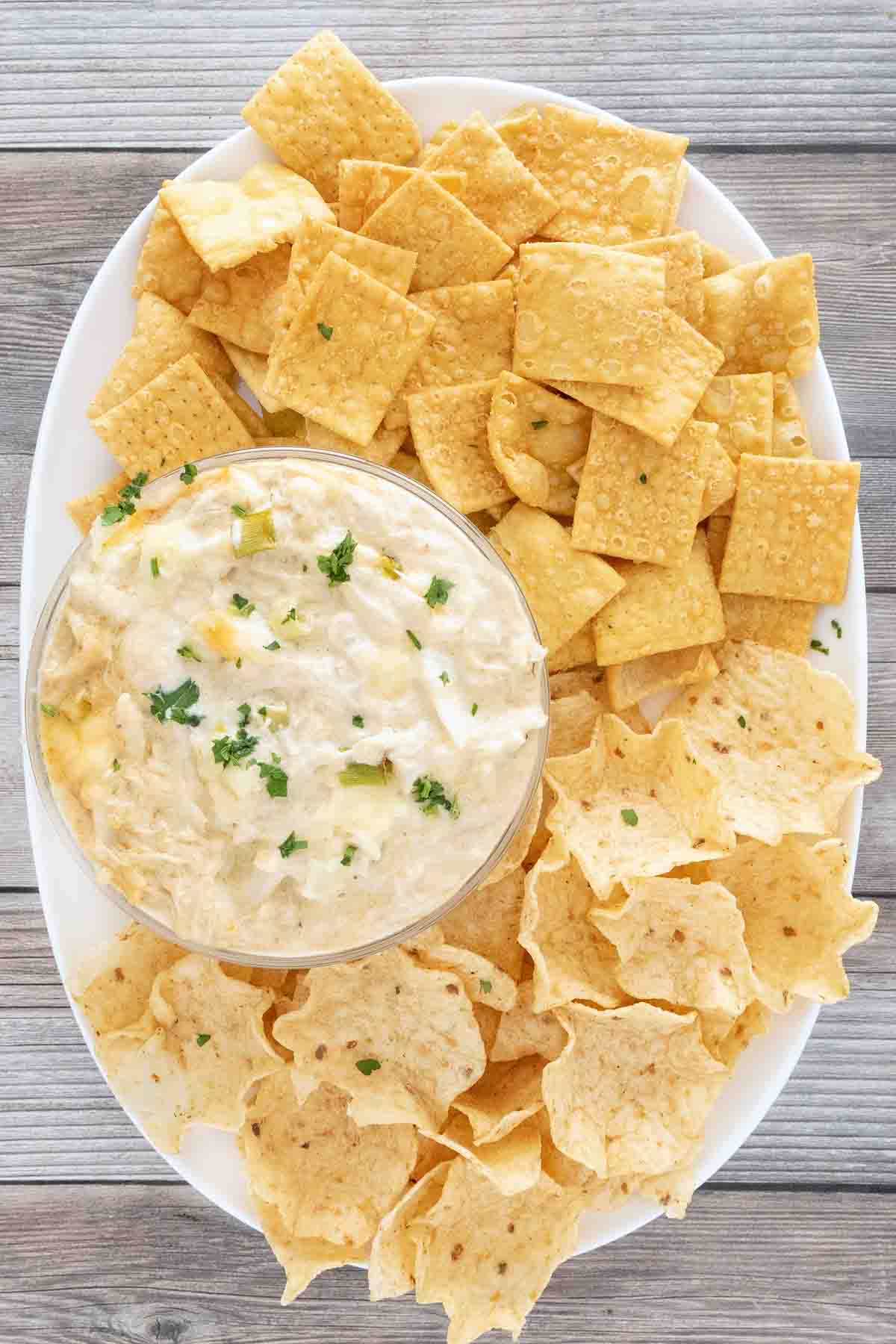 crab rangoon dip in bowl on a white platter with crackers and tortilla dippers.