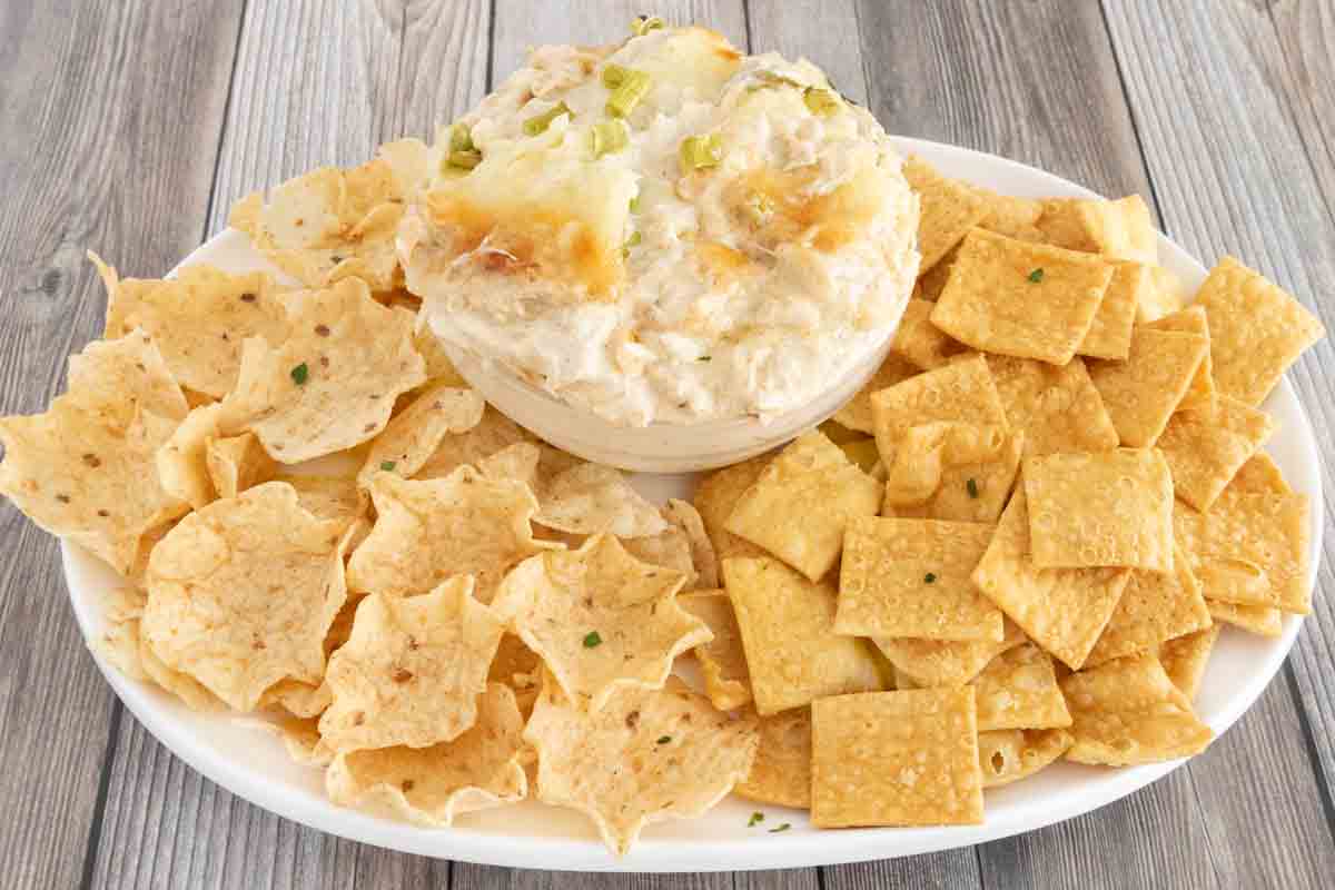 crab rangoon dip in bowl on a white platter with crackers and tortilla dippers.