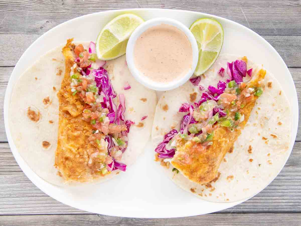 Cod fish tacos with fish taco sauce on a white platter.