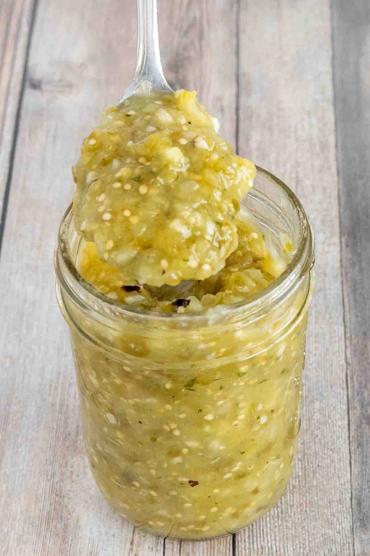 Mexican Salsa Verde in a glass jar with a spoon coming out.