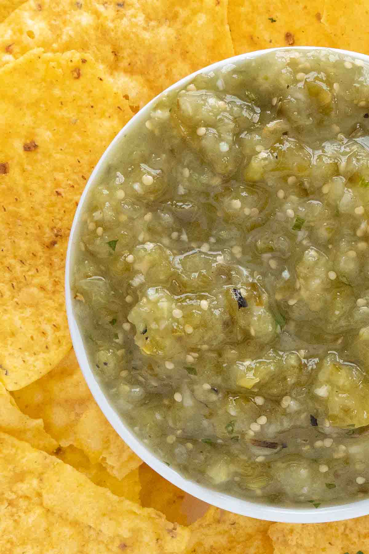 Mexican salsa verde in a white bowl with tortilla chips on a white platter.