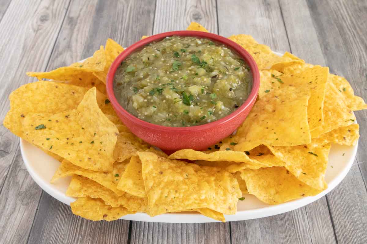 Mexican salsa verde in a red bowl with tortilla chips on a white platter.