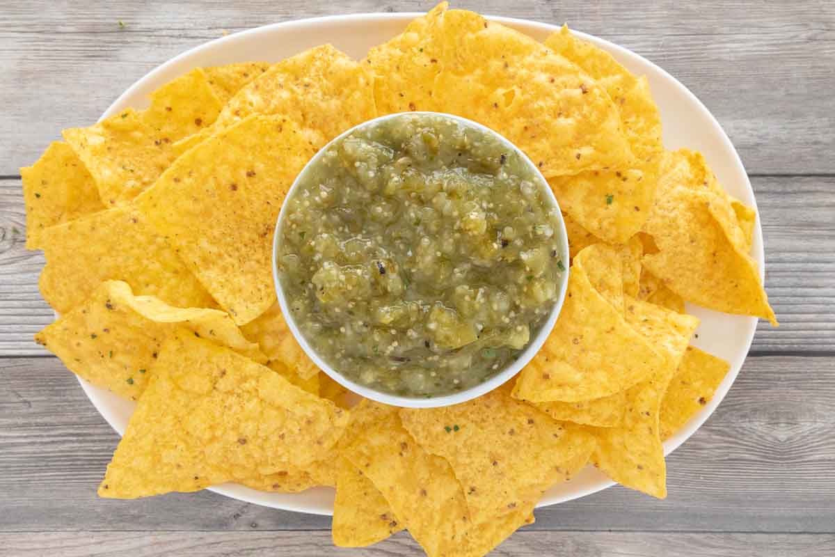 Mexican salsa verde in a red bowl with tortilla chips on a white platter.