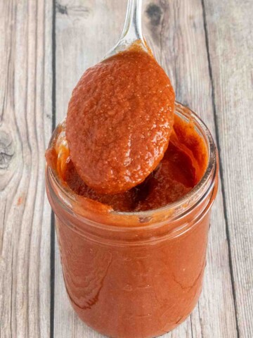 Taco sauce in a glass jar with a spoon coming out.