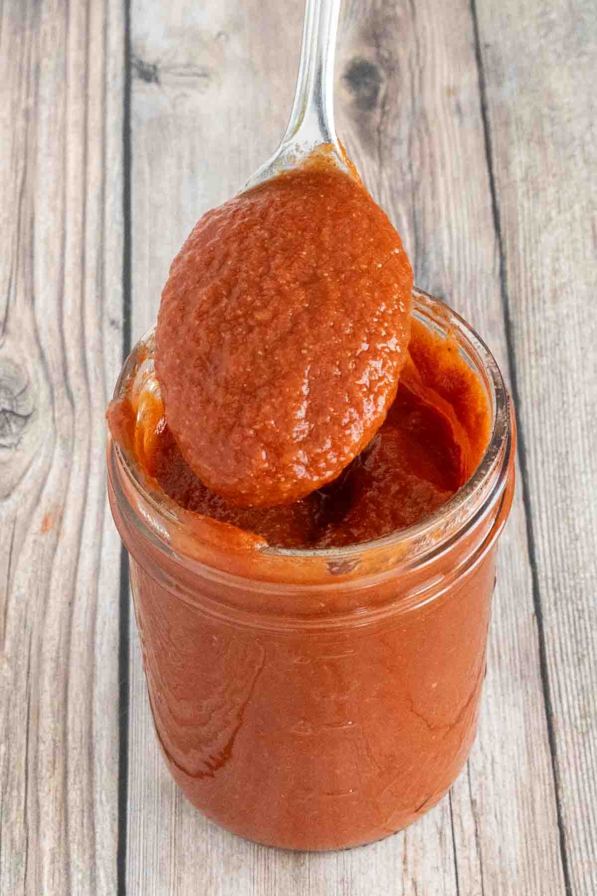 Taco sauce in a glass jar with a spoon coming out.