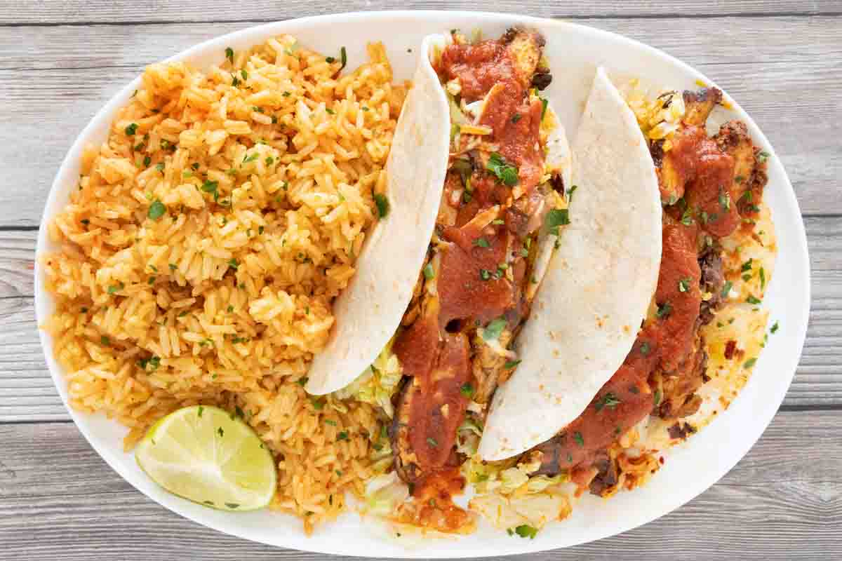 Tacos with taco sauce on a white platter with rice.