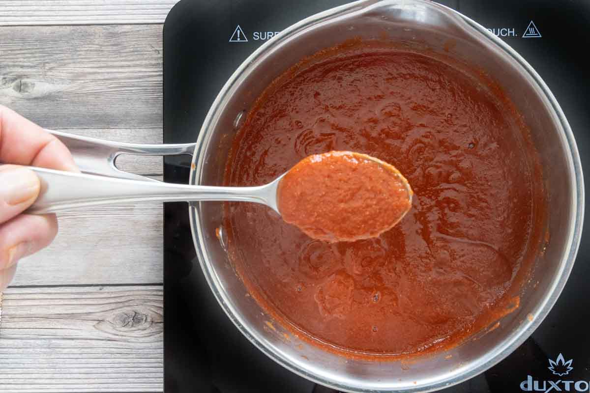 A spoon coming out of a saucepan of taco sauce.