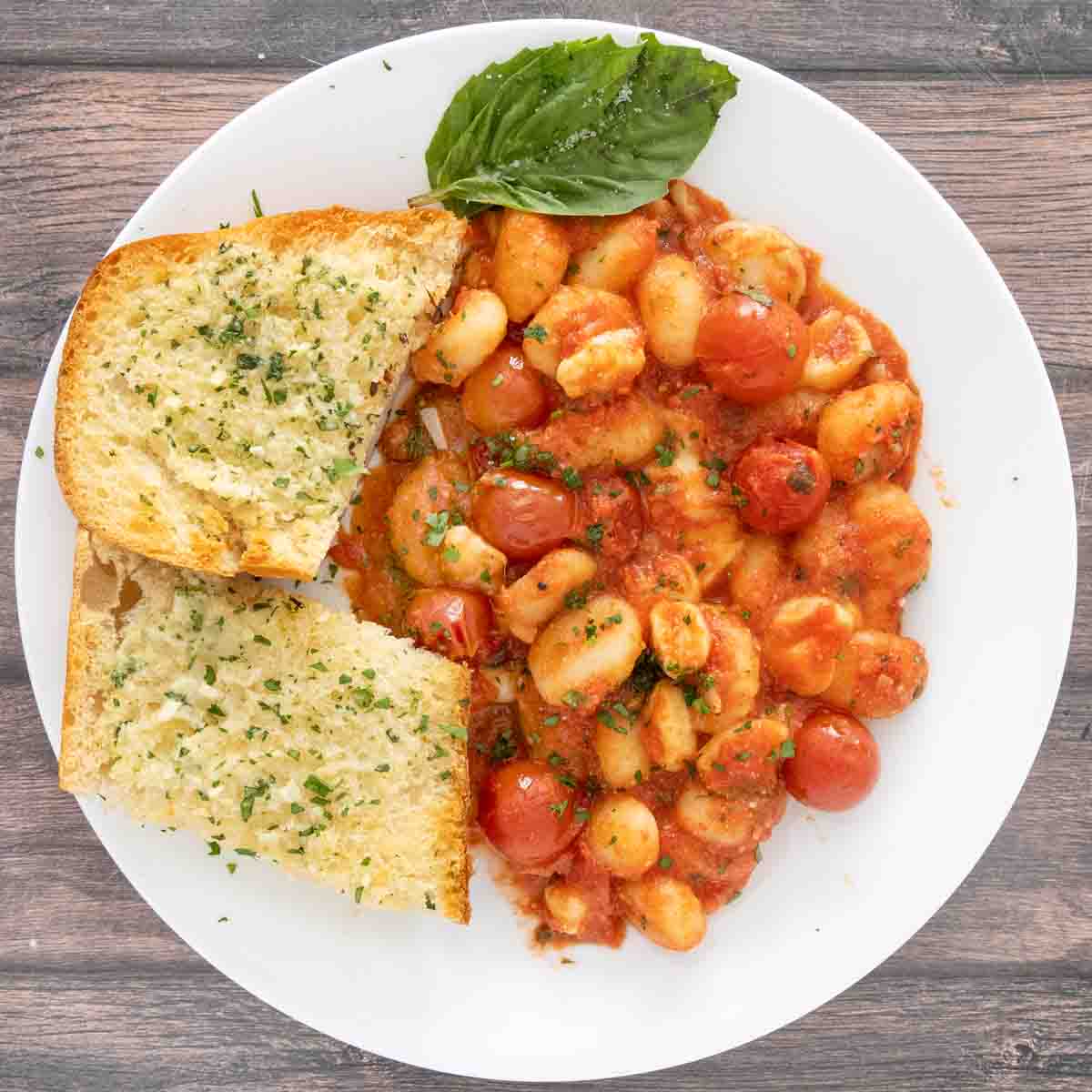 Garlic bread with gnocchi sorrentina on a white plate.